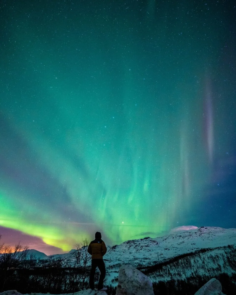 Nordlysfotografering med en person foran et snødekt landskap