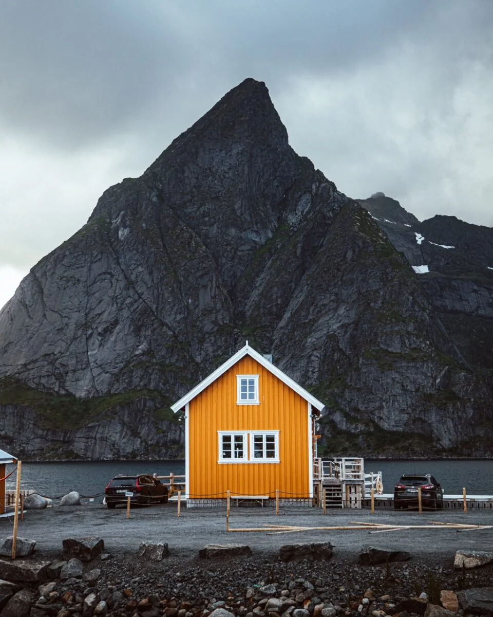 Gult hus ved vannet med et bratt fjell i bakgrunnen