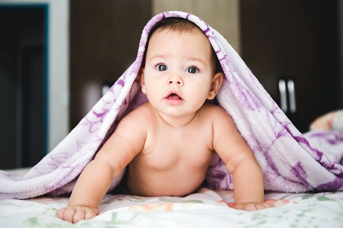 Baby under et lyst teppe med blikket vendt mot kameraet